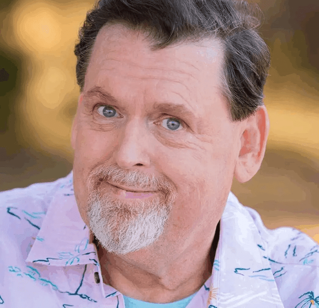 Portrait of a smiling middle-aged man with blue eyes and a gray beard.